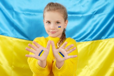 Photo of Little girl with paint on hands and face near Ukrainian flag