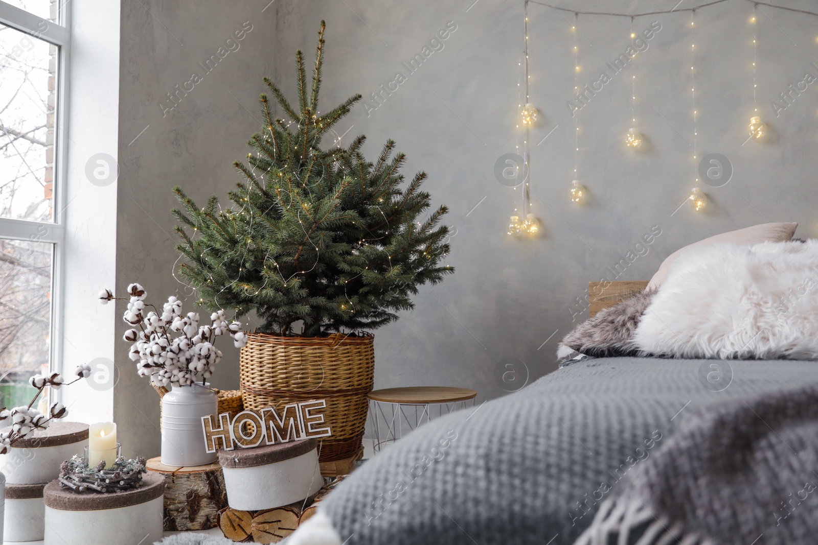 Photo of Little Christmas tree with fairy lights in bedroom interior