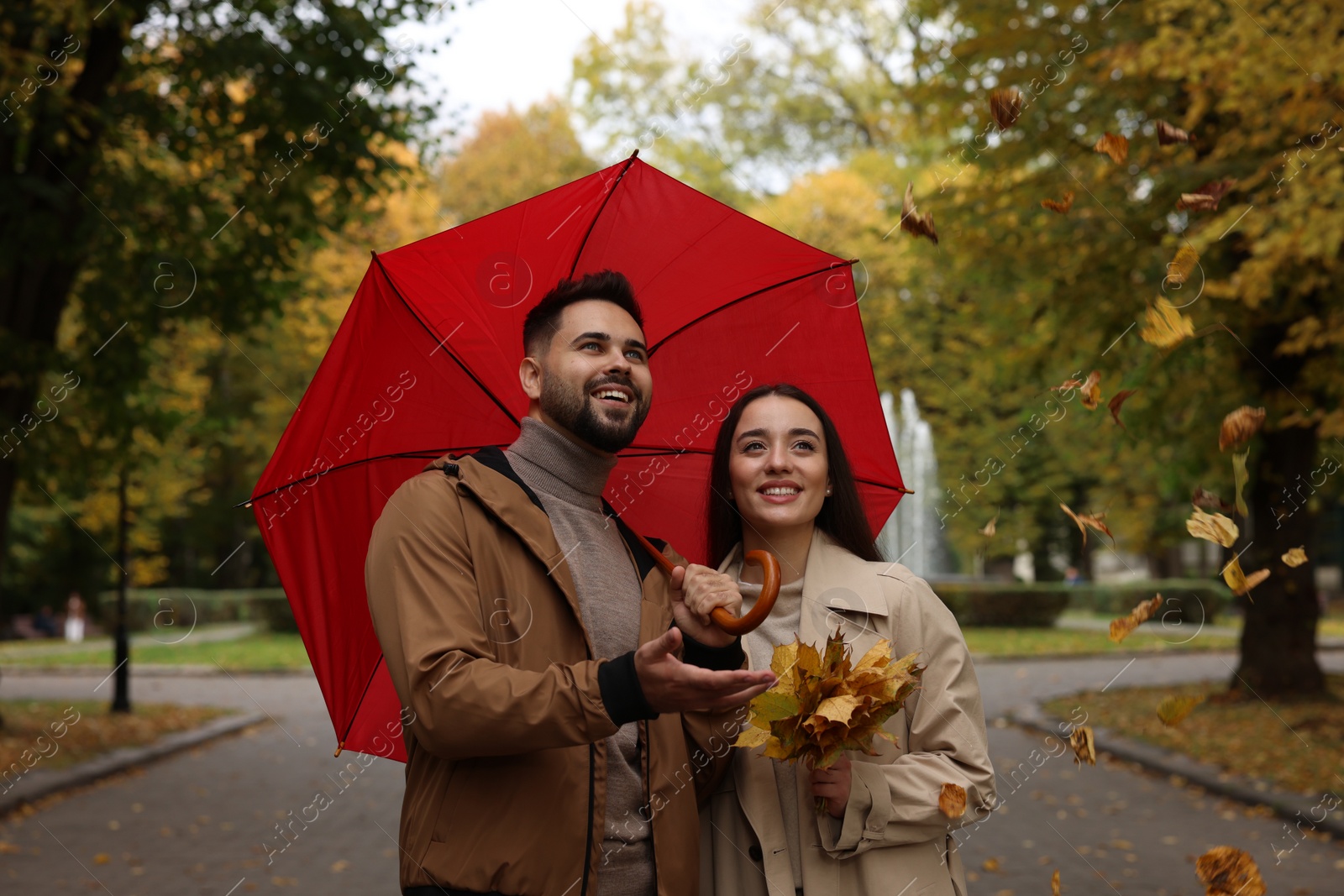 Photo of Happy young couple with red umbrella spending time together in autumn park