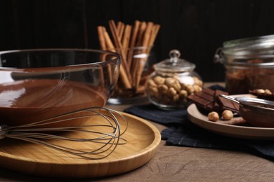Photo of Bowl of chocolate cream with whisk and ingredients on wooden table