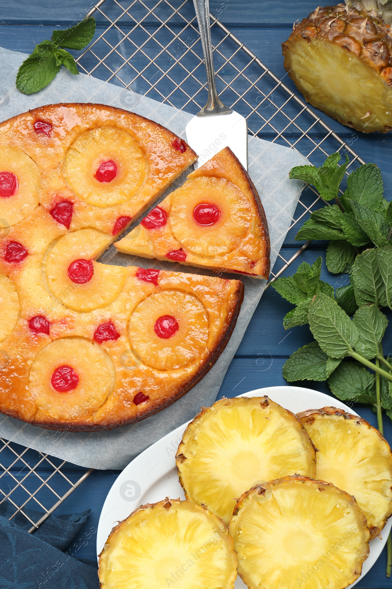 Photo of Delicious cut pineapple pie with cherry and mint on blue wooden table, flat lay