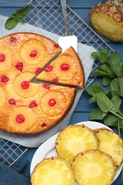 Delicious cut pineapple pie with cherry and mint on blue wooden table, flat lay