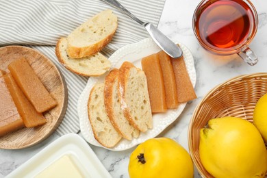 Photo of Delicious quince paste, bread, butter, cup of tea and fresh fruits on white marble table, flat lay