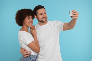 International dating. Happy couple taking selfie on light blue background