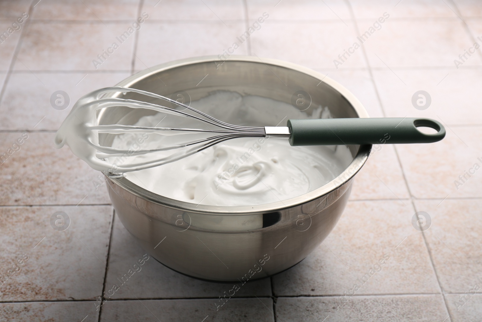 Photo of Bowl and whisk with whipped cream on tiled table