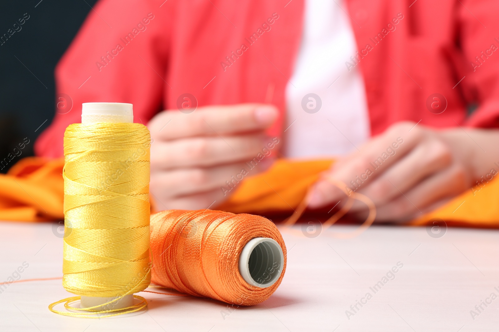 Photo of Woman sewing cloth with needle at light wooden table, focus on spools of threads