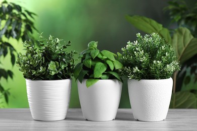Photo of Different artificial potted herbs on white wooden table outdoors