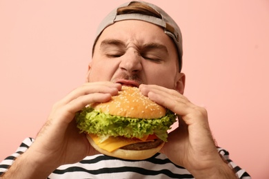 Young man eating tasty burger on color background