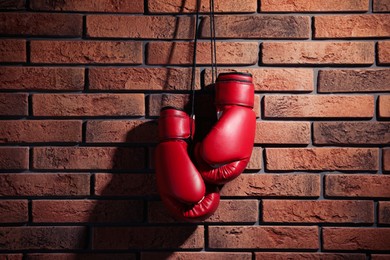 Photo of Pair of red boxing gloves hanging on brick wall