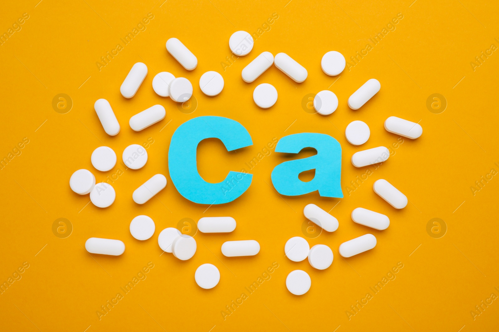 Photo of Pills and calcium symbol made of light blue letters on orange background, flat lay