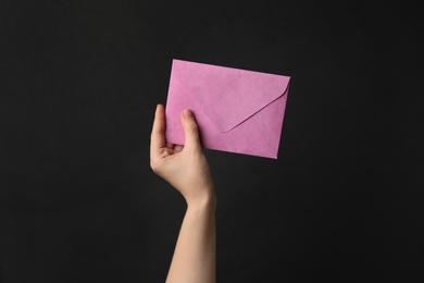 Woman holding pink paper envelope on black background, closeup
