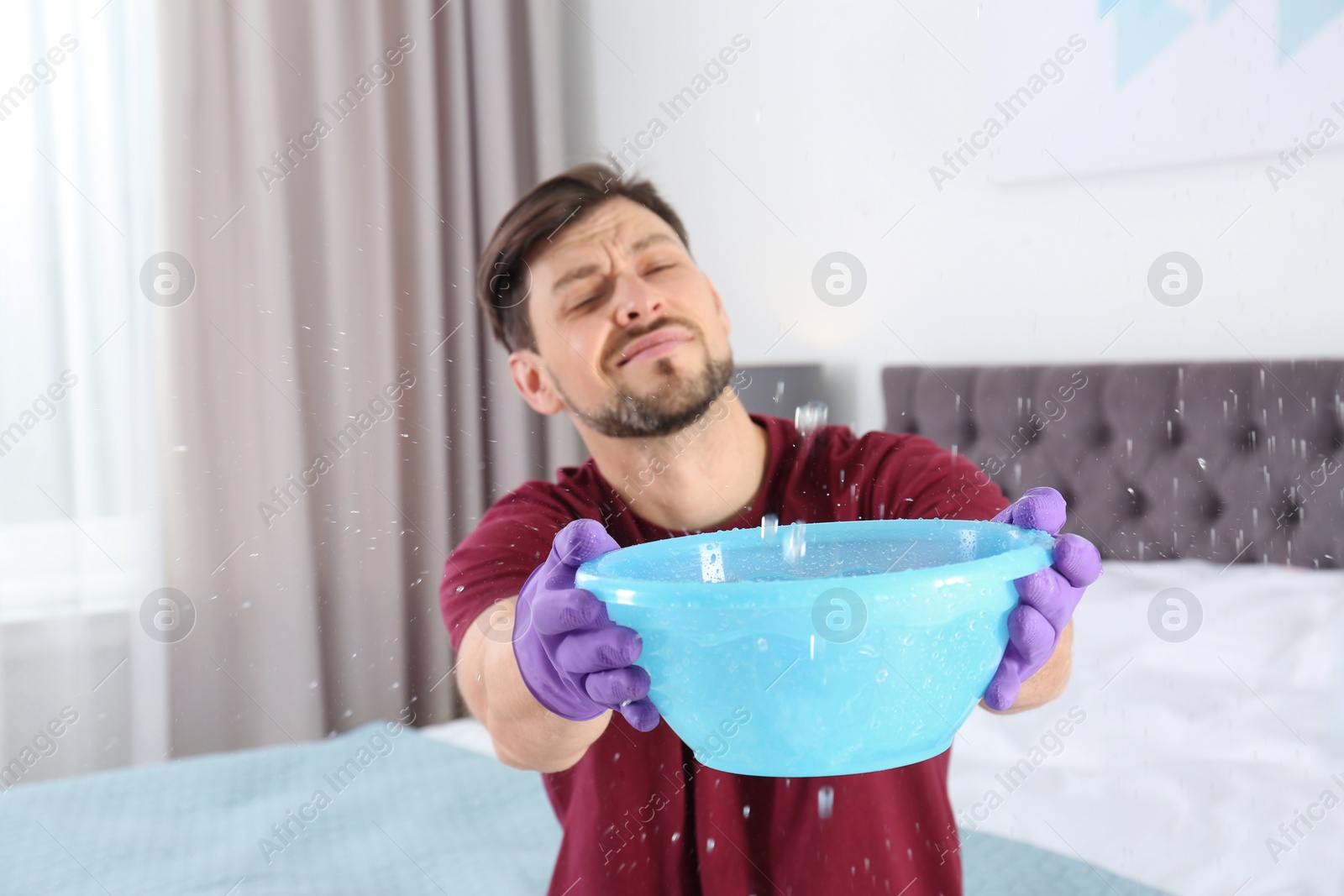 Photo of Man collecting leaking water from ceiling in bedroom. Time to call plumber