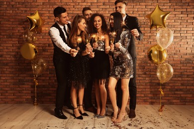 Happy friends with glasses of sparkling wine and sparklers celebrating New Year indoors