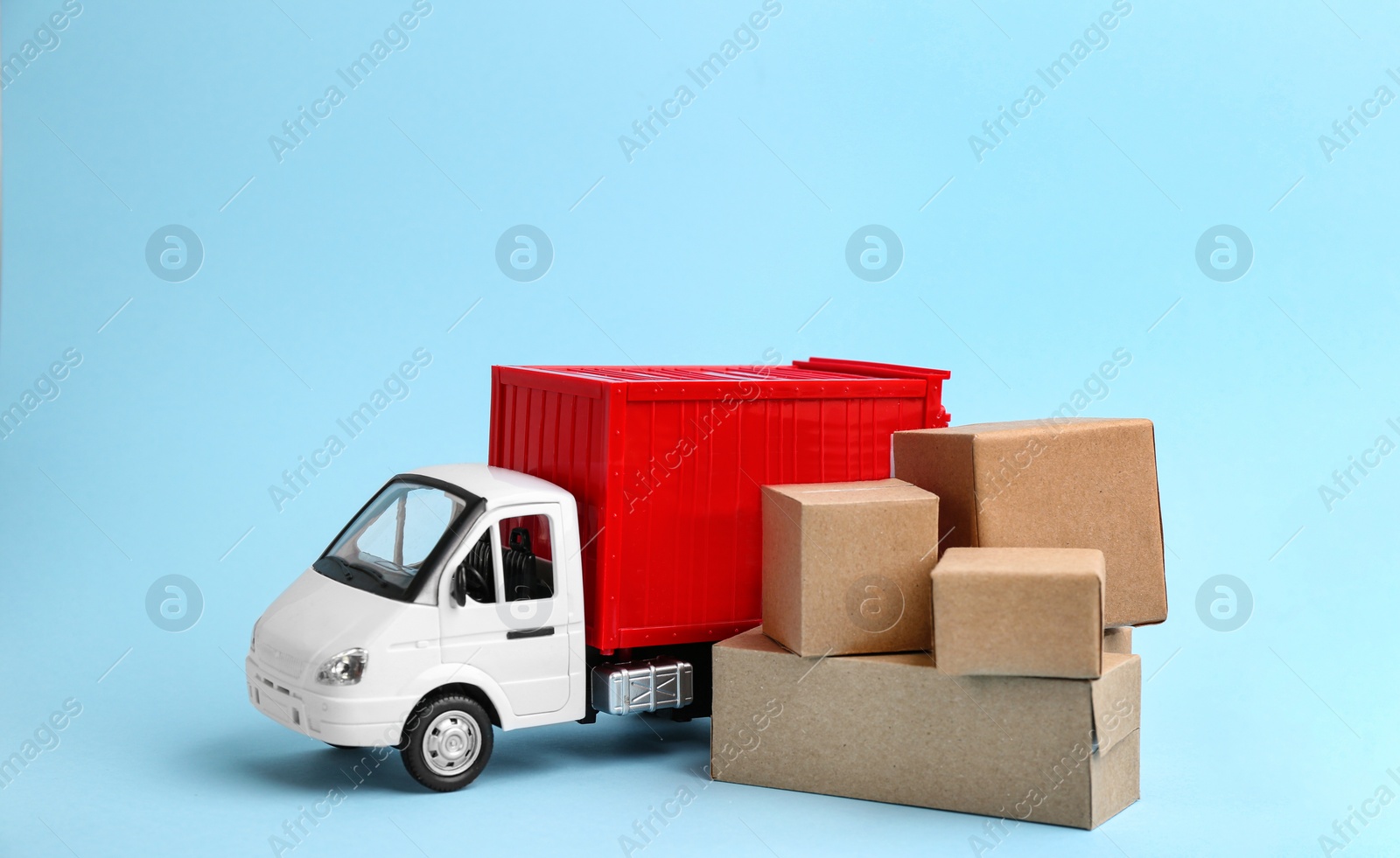 Photo of Truck model and carton boxes on light blue background. Courier service