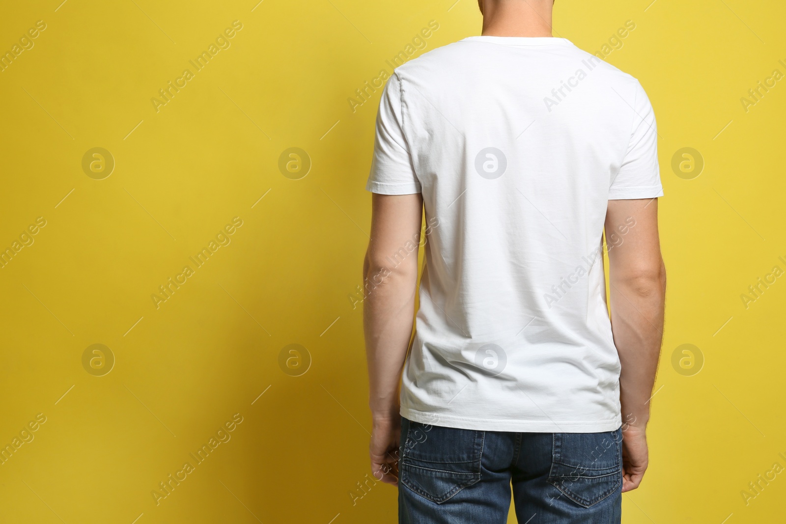 Photo of Back view of young man wearing blank t-shirt on yellow background, closeup. Mockup for design