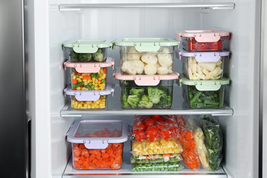 Plastic bags and containers with different frozen vegetables in refrigerator