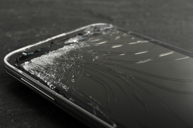 Photo of Smartphone with cracked screen on black table, closeup. Device repair