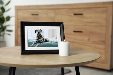 Frame with picture of dog and burning candle on wooden table indoors. Pet funeral