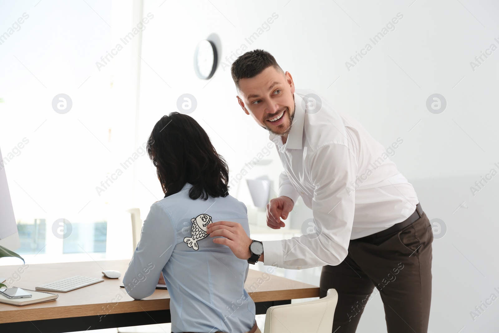 Photo of Man sticking paper fish to colleague's back in office. April fool's day