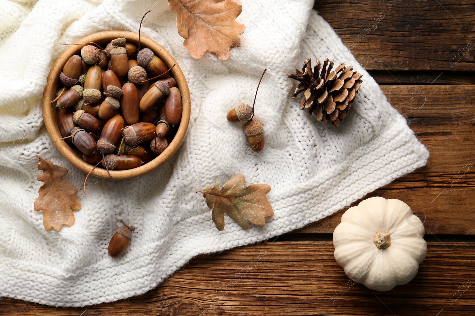 Photo of Flat lay composition with acorns, pumpkin and white knitted fabric on wooden table