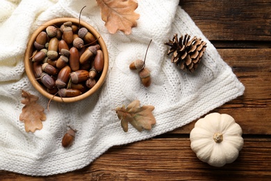 Photo of Flat lay composition with acorns, pumpkin and white knitted fabric on wooden table