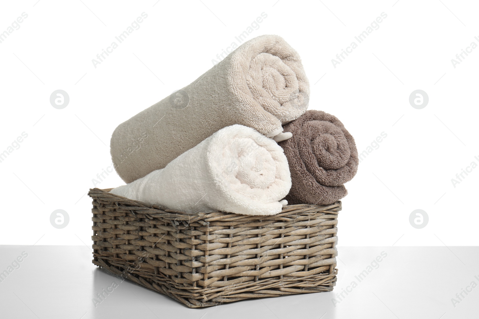 Photo of Rolled soft terry towels in wicker basket on white background