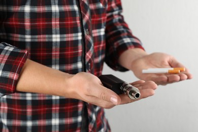 Photo of Man with cigarettes and vaping device on light background, closeup. Smoking alternative