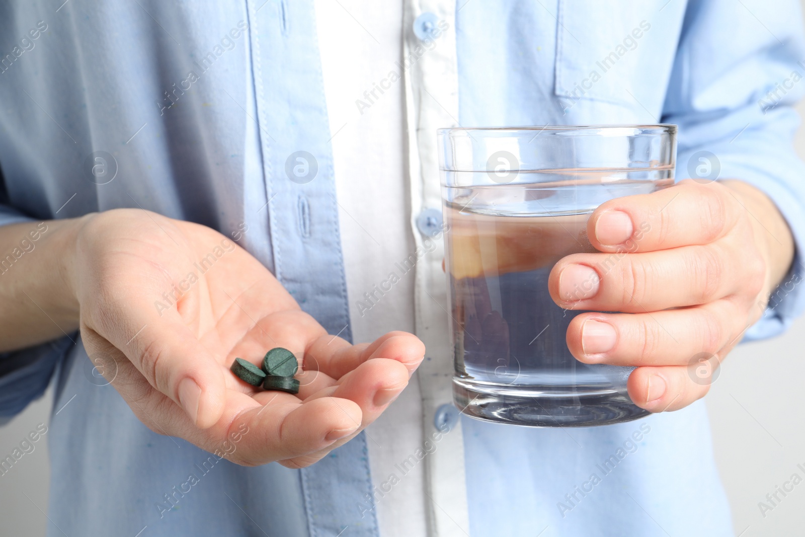 Photo of Woman holding spirulina pills and glass of water, closeup