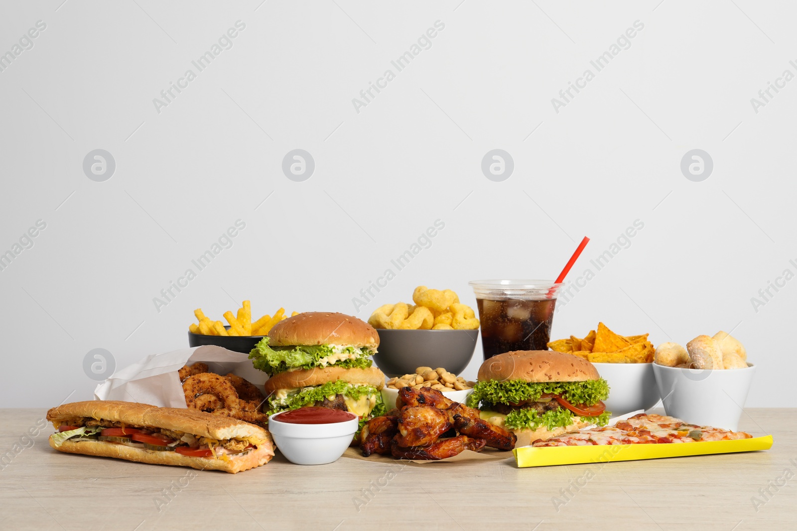 Photo of French fries, burgers and other fast food on wooden table against white background