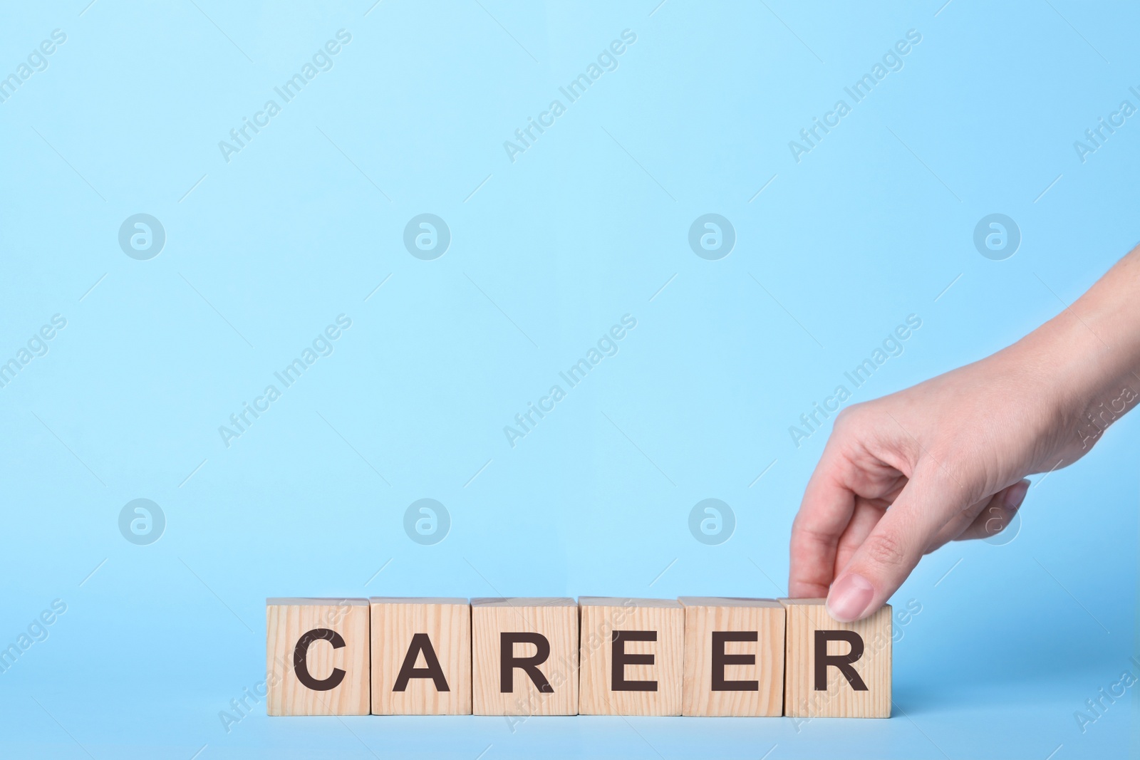 Photo of Woman making word CAREER with wooden cubes on light blue background, closeup. Space for text