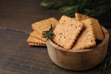 Photo of Cereal crackers with flax, sesame seeds and rosemary in bowl on wooden table, closeup. Space for text