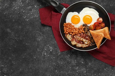 Photo of Frying pan with cooked traditional English breakfast on black textured table, top view. Space for text