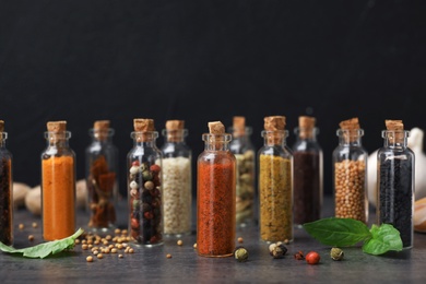 Glass bottles with different spices on table against black background