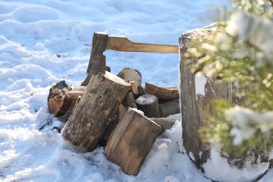 Metal axe in wooden log and pile of wood outdoors on sunny winter day