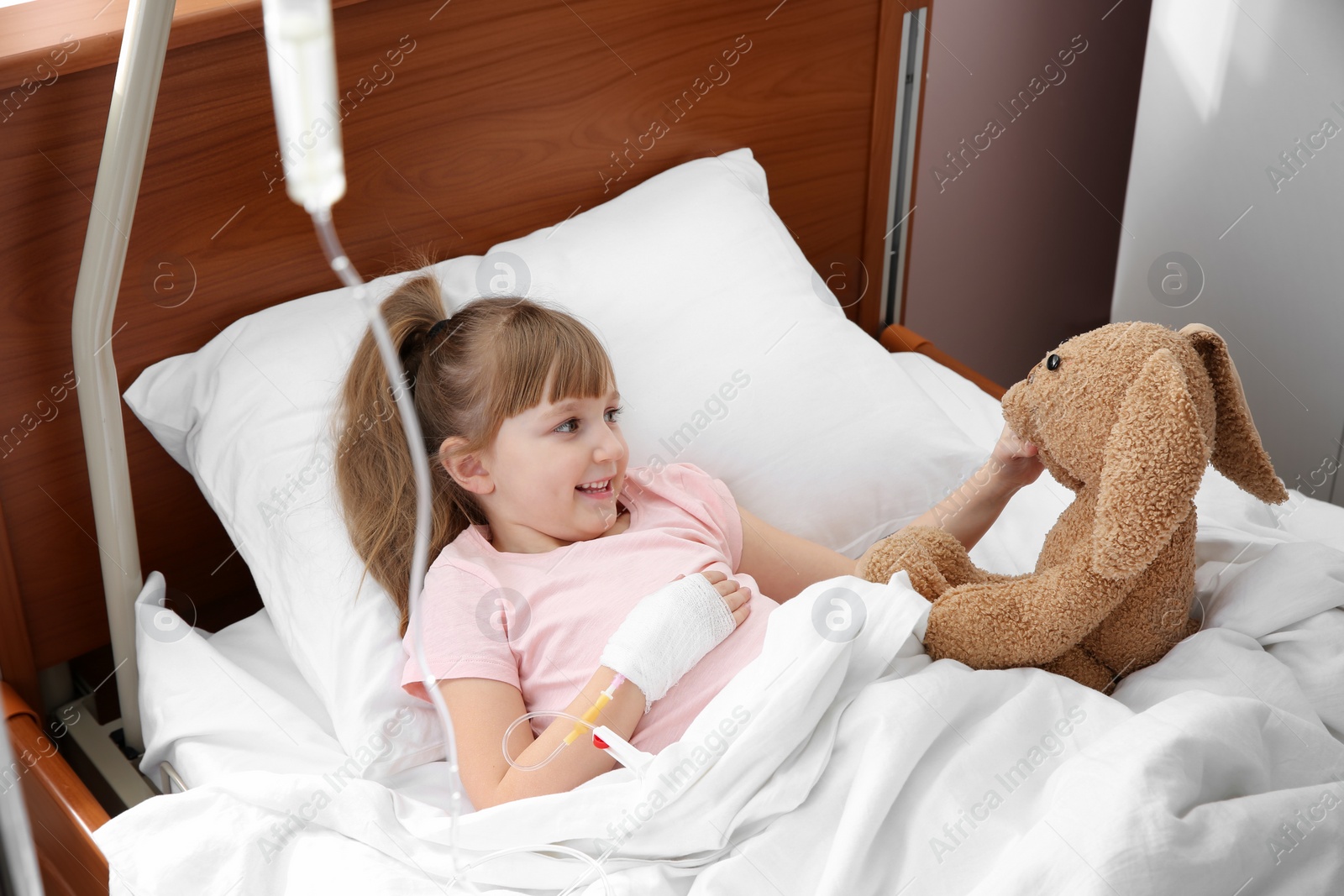 Photo of Little child with intravenous drip and toy in hospital bed