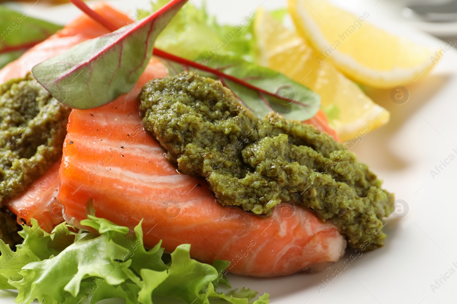 Photo of Tasty cooked salmon with pesto sauce on plate, closeup