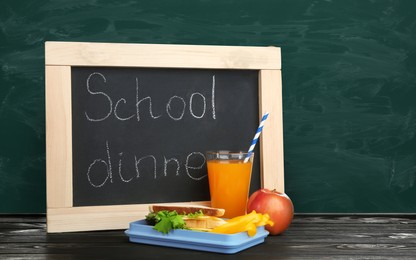 Image of Lunch box with food and small blackboard on wooden table near green chalkboard