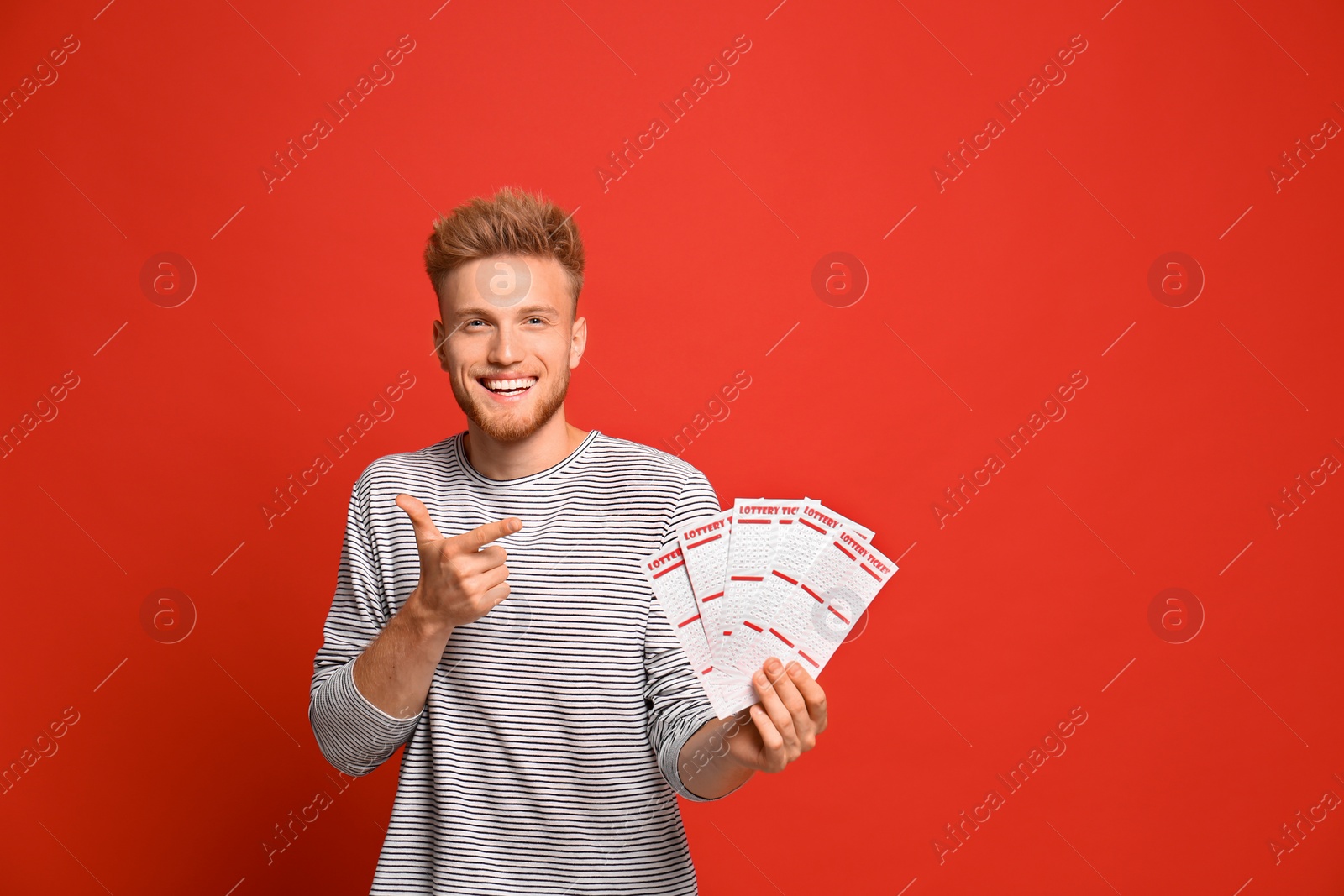 Photo of Portrait of happy young man with lottery tickets on red background