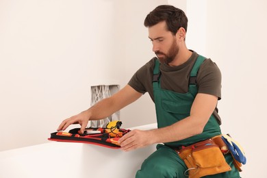 Electrician taking screwdriver from tool bag indoors