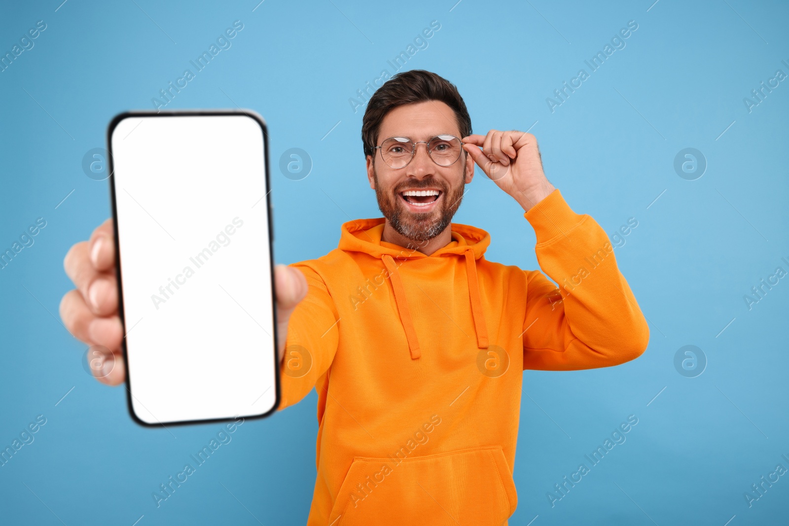 Photo of Handsome man showing smartphone in hand on light blue background