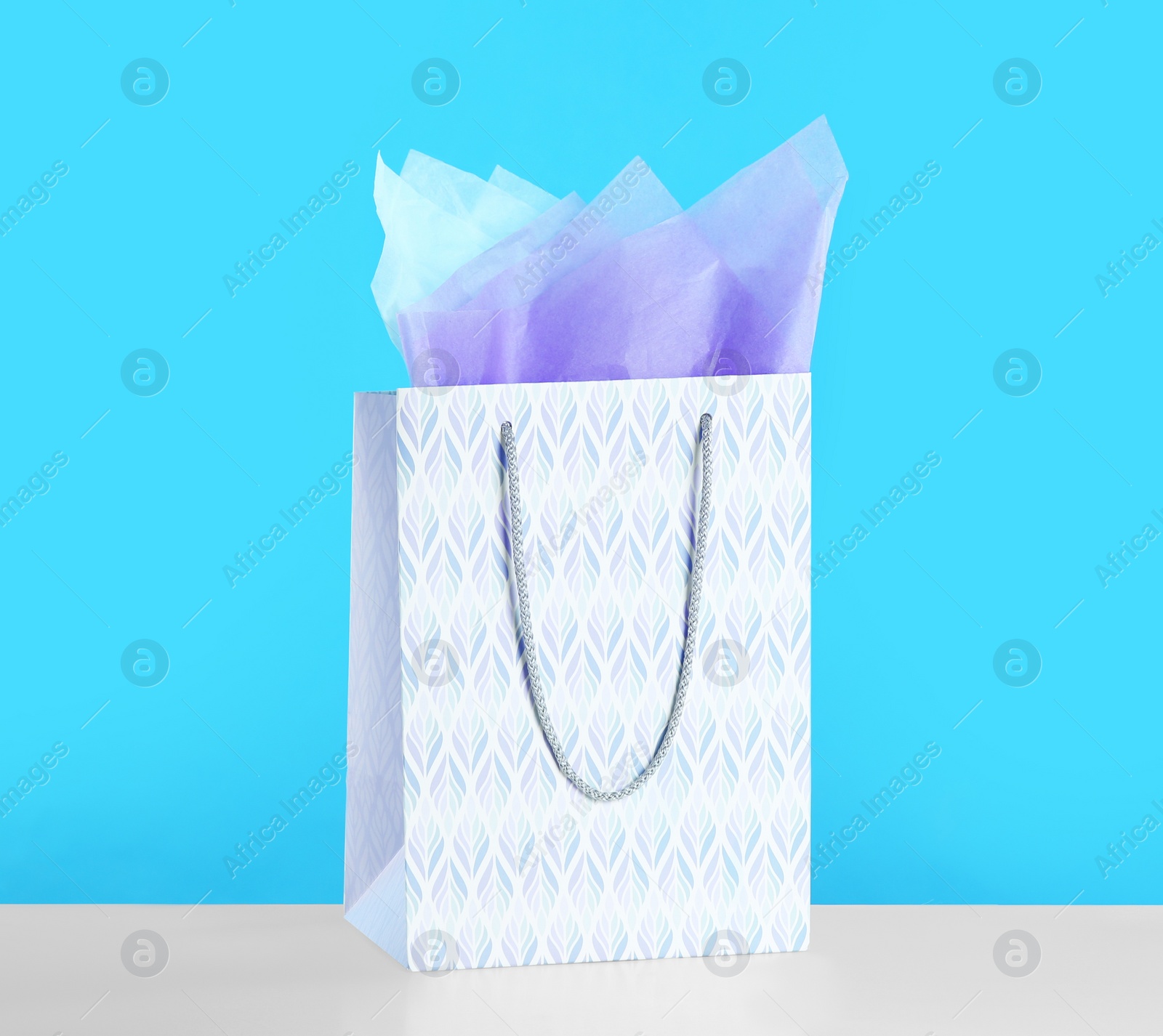 Photo of Gift bag with paper on white table against light blue background