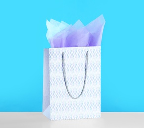 Photo of Gift bag with paper on white table against light blue background