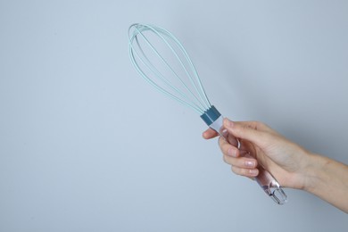 Photo of Woman holding whisk on light grey background, closeup. Space for text