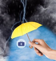 Image of Insurance agent protecting medical kit illustration with yellow umbrella from thunderstorm, closeup
