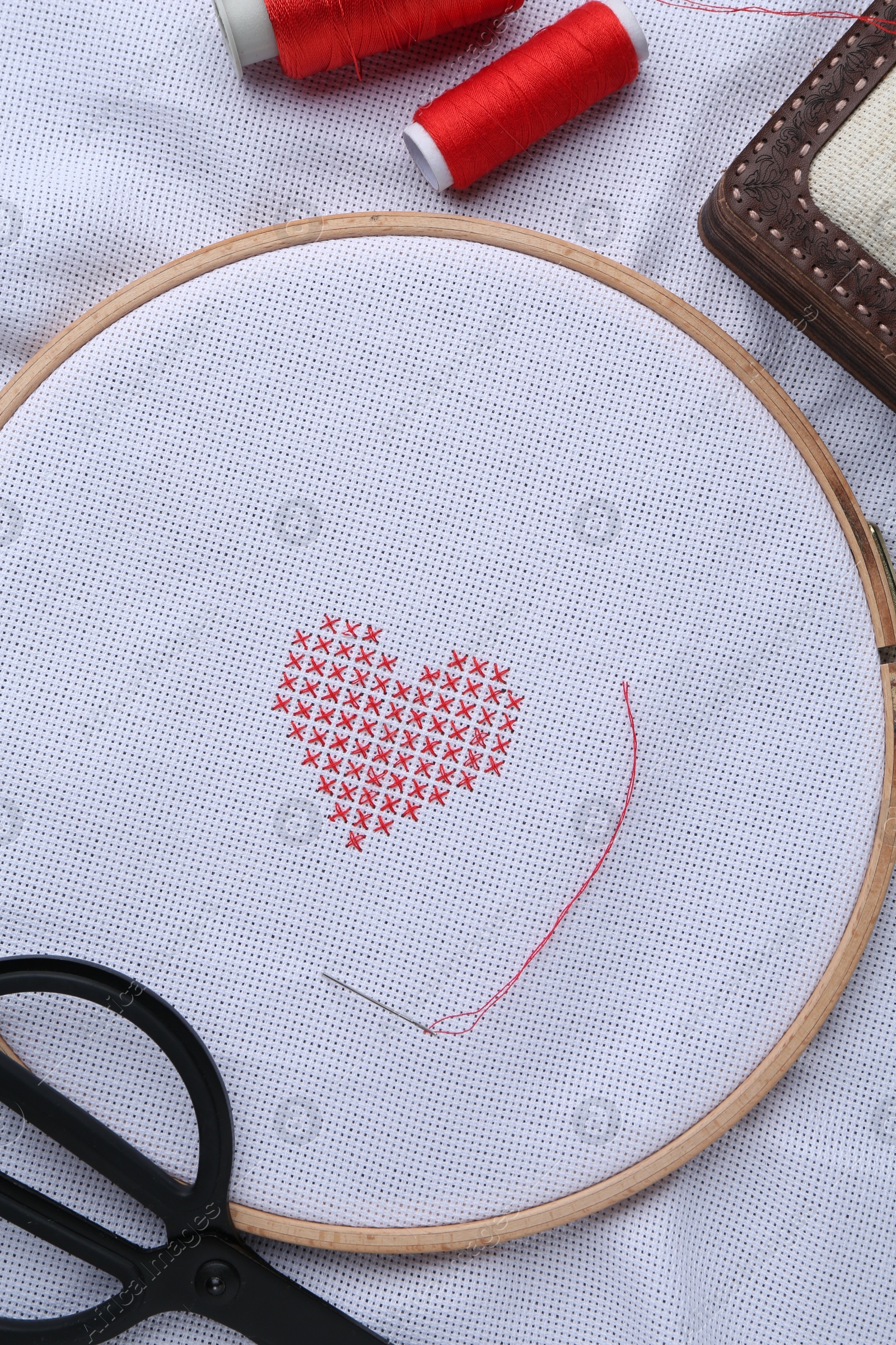 Photo of Embroidered red heart, needle and scissors on white cloth, top view