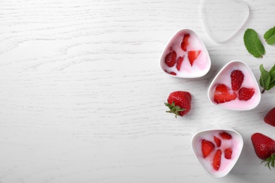 Cups of homemade yogurt and strawberries on white table, flat lay with space for text. Recipe for multi cooker