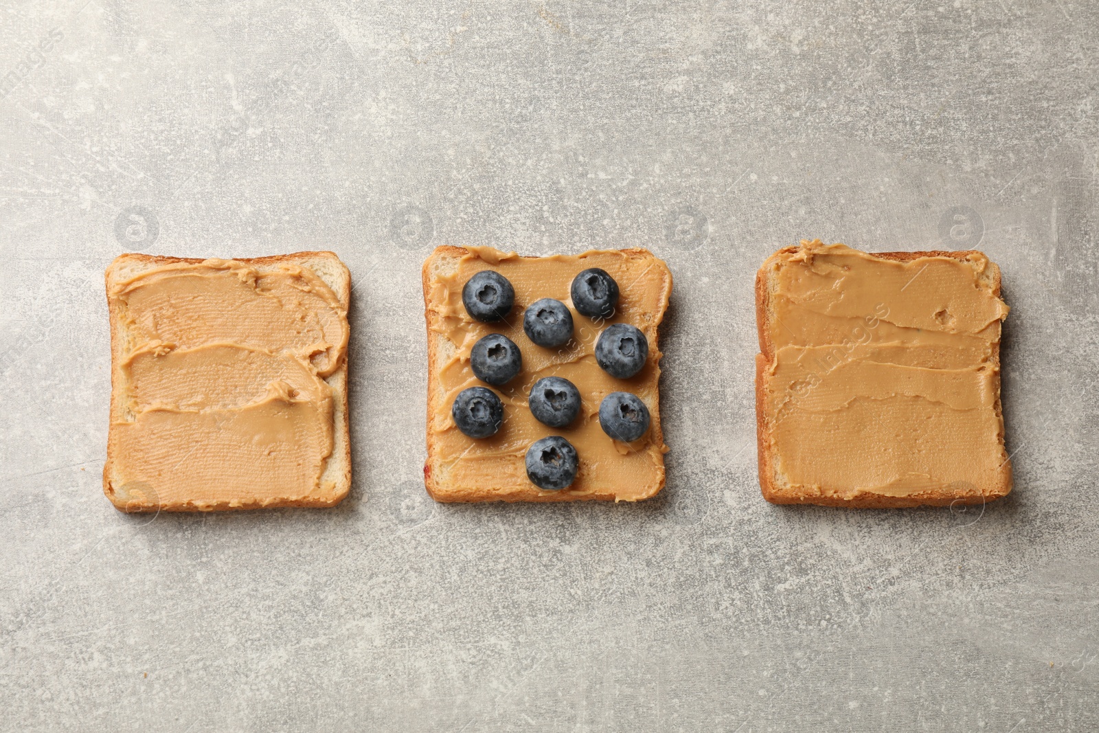 Photo of Tasty peanut butter sandwiches with fresh blueberries on gray table, flat lay