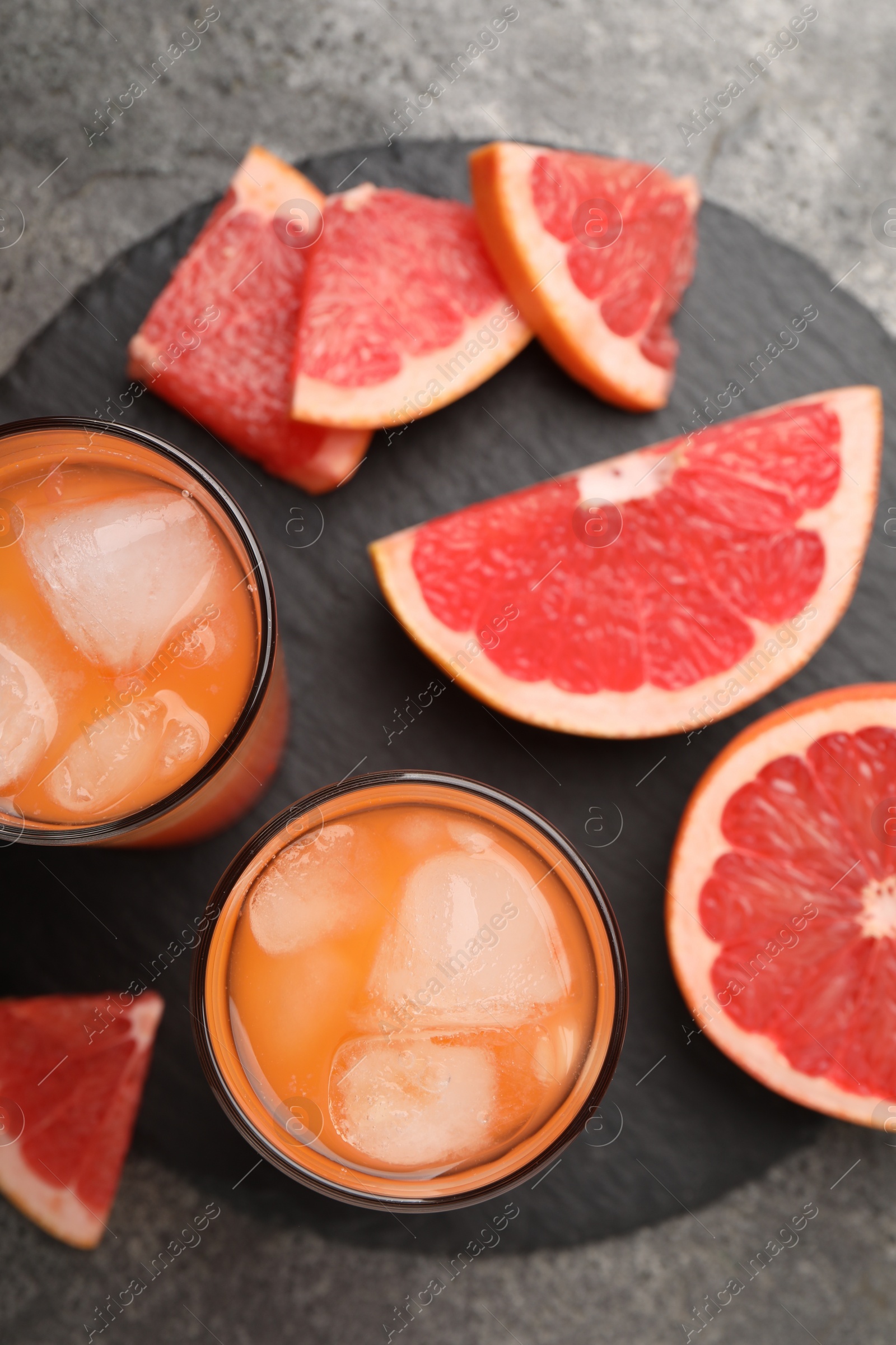 Photo of Tasty grapefruit drink with ice in glasses and fresh fruits on dark textured table, flat lay