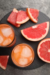 Tasty grapefruit drink with ice in glasses and fresh fruits on dark textured table, flat lay