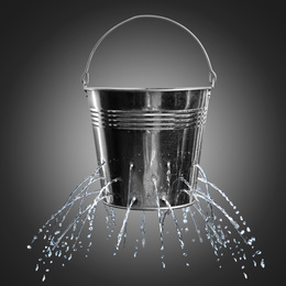 Leaky bucket with water on dark background 